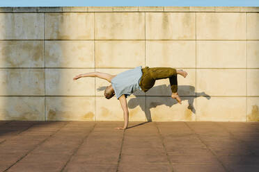 Männlicher Tänzer balanciert auf einer Hand vor einer Wand - XLGF02066