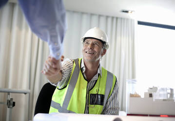 Mann in reflektierender Kleidung beim Händeschütteln mit einem Kollegen im Büro - AJOF01471