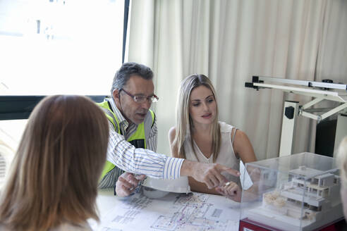 Männlicher Architekt zeigt Kollegen ein Modell während einer Besprechung im Büro - AJOF01484