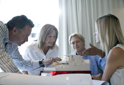 Male and female professionals looking at architectural model in office - AJOF01486