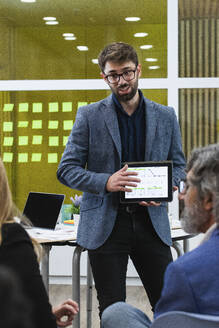 Junger Geschäftsmann erklärt männlichen und weiblichen Mitarbeitern bei einer Besprechung im Büro die Geschäftsstrategie - PNAF01840