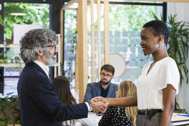 Smiling male and female entrepreneurs shaking hands with coworkers in meeting at office - PNAF01850