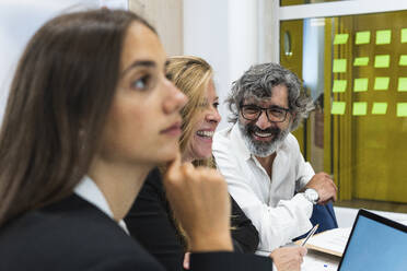 Glückliche männliche und weibliche Fachkräfte lächelnd bei einer Geschäftsfrau, die im Büro nachdenkt - PNAF01852