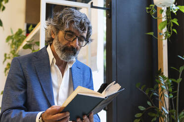 Älterer Geschäftsmann mit Brille liest Tagebuch im Büro - PNAF01853