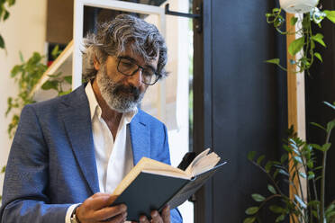 Senior businessman wearing eyeglasses reading diary at office - PNAF01853