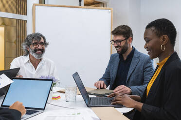 Lächelnde männliche und weibliche Unternehmer diskutieren bei der Arbeit am Tisch im Büro - PNAF01867