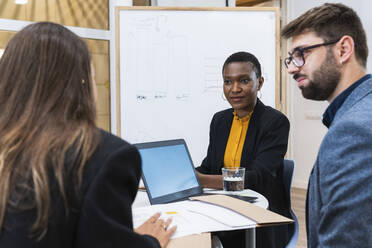 Männliche und weibliche Fachleute betrachten eine Geschäftsfrau, die während einer Besprechung im Büro diskutiert - PNAF01872