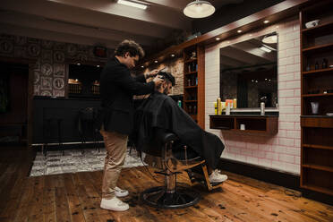 Männlicher Friseur, der einem Kunden im Friseursalon die Haare schneidet - ACPF01259
