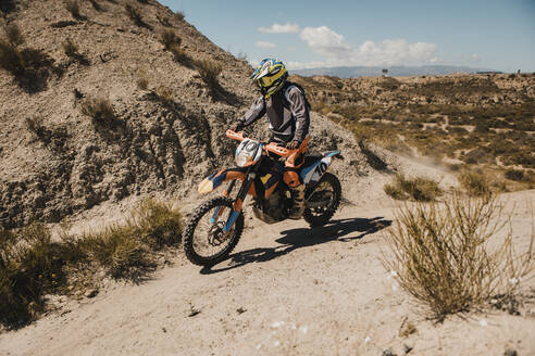 Male biker in protective sportswear riding motorcycle on dirt road - DMGF00556