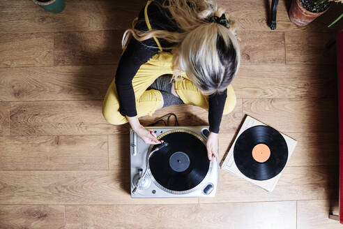 Woman using turntable while sitting on floor - ASGF00467