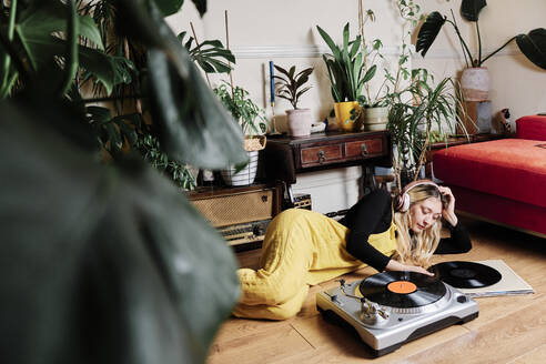 Woman with headphones listening music while relaxing on floor at home - ASGF00472