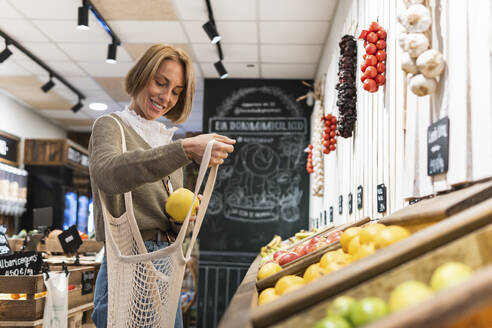 Woman collecting fruit in mesh bag while shopping in supermarket - PNAF01915