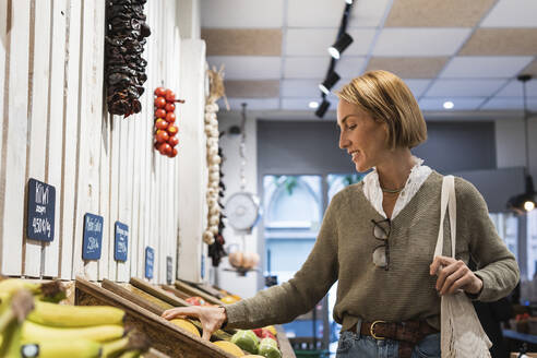 Woman checking fruit kept in retail display at supermarket - PNAF01916