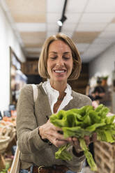 Woman smiling while holding vegetable in supermarket - PNAF01918