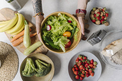 Mann hält Salatschüssel mit Gemüse und Obst auf dem Tisch - EYAF01638