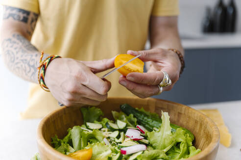 Man cutting yellow tomato while preparing salad in kitchen - EYAF01641