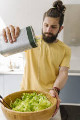 Mann gibt Olivenöl in eine Salatschüssel zu Hause - EYAF01645