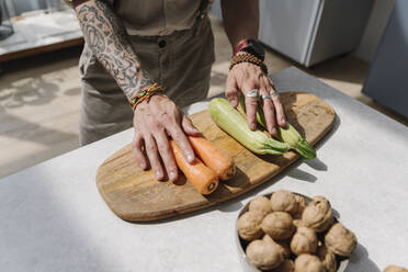 Man standing by vegetable and cutting board on kitchen island at home - EYAF01653