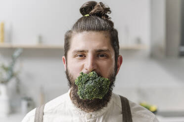Mittlerer erwachsener Mann starrt mit Brokkoli im Mund nach Hause - EYAF01657