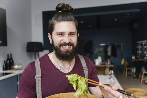 Lächelnder Mann isst Salat in der Küche zu Hause - EYAF01662