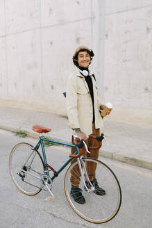 Smiling man holding bicycle handlebar while standing on footpath - AGGF00109