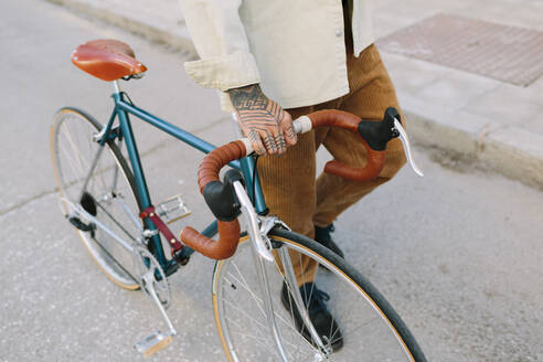 Tattooed man wheeling bicycle on road - AGGF00111