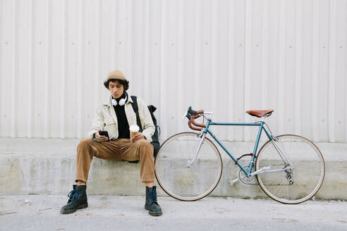 Man using mobile phone while sitting by bicycle - AGGF00112