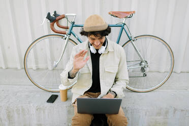 Smiling male professional waving at laptop during video call - AGGF00115