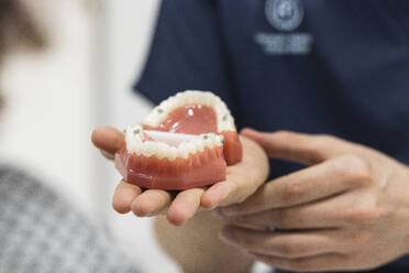 Mature female dentist showing dentures to patient in clinic - PNAF01938