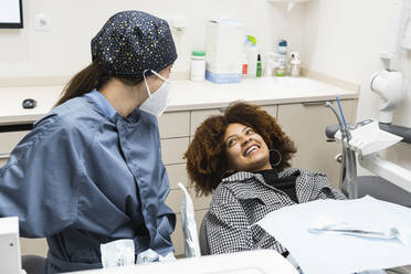 Afro female patient smiling at dentist wearing protective face mask in clinic - PNAF01952