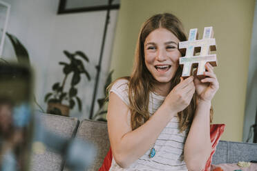 Lächelndes Teenager-Mädchen hält Hashtag-Symbol beim Filmen zu Hause - MFF08027