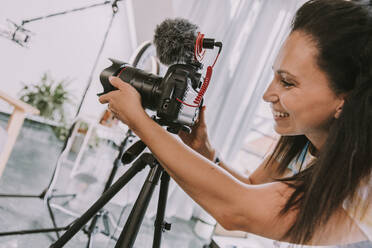 Lächelnde Frau beim Einstellen der Kamera während der Dreharbeiten im Studio - MFF08047