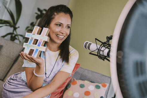 Smiling woman holding hashtag symbol while vlogging at home - MFF08052