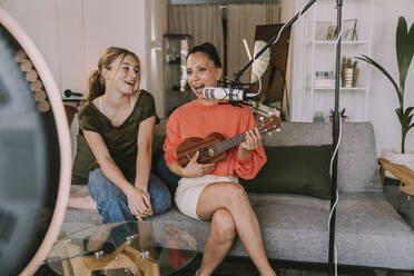 Mädchen sitzt mit Freundin auf dem Sofa und spielt Ukulele zu Hause - MFF08123