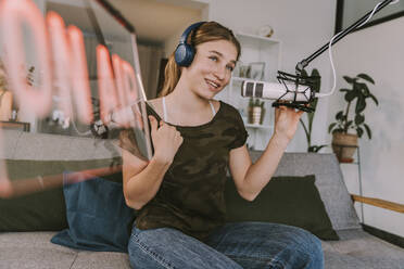 Teenage girl speaking on microphone while broadcasting at home - MFF08132