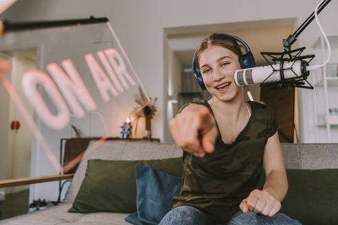 Smiling teenage girl pointing while broadcasting at home - MFF08134