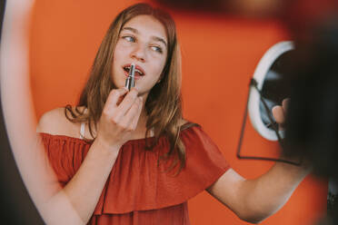 Female influencer applying lipstick while vlogging make-up tutorial at home - MFF08184