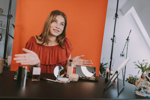 Teenage girl filming gesturing while vlogging make-up tutorial at home - MFF08189