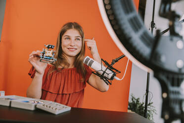 Lächelndes Teenager-Mädchen, das ein Robotermodell hält, während es zu Hause vloggt - MFF08193