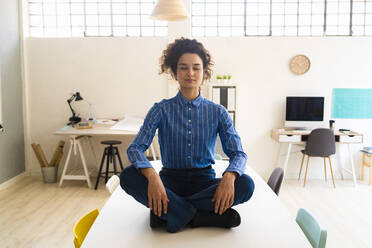 Geschäftsfrau übt Yoga im Schneidersitz auf dem Schreibtisch im Büro - GIOF12871