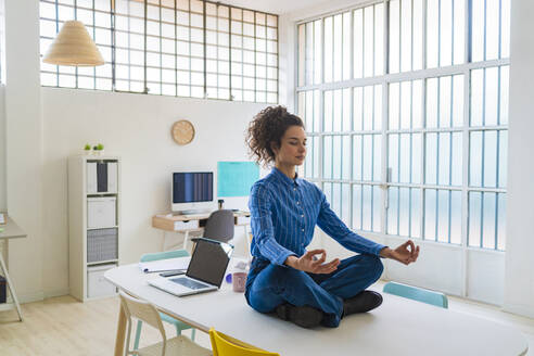 Female entrepreneur meditating while sitting in office - GIOF12873