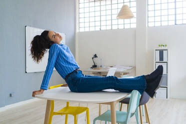 Junge Geschäftsfrau mit übereinander geschlagenen Beinen im Büro sitzend und nachdenklich - GIOF12875