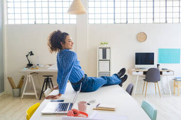 Female entrepreneur sitting by laptop on desk in office - GIOF12876