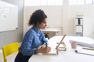 Female entrepreneur with note pad looking at digital tablet in office - GIOF12888