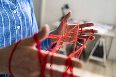 Female entrepreneur making cats cradle with woolen string in office - GIOF12899