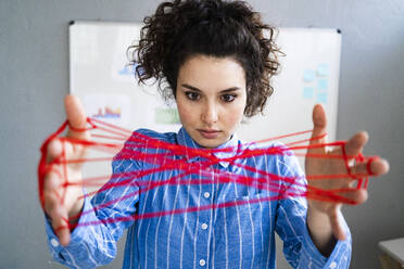 Female entrepreneur looking at woolen cats cradle in hand - GIOF12901