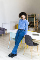 Lächelnde Geschäftsfrau, die sich in einem kreativen Büro auf den Schreibtisch stützt - GIOF12902