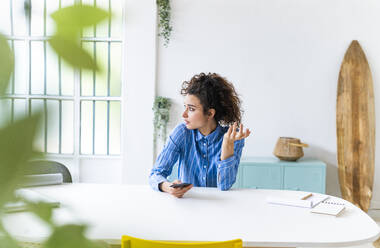 Businesswoman with mobile phone looking away in creative office - GIOF12905