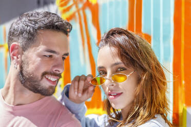 Lächelnder Mann schaut Frau mit Sonnenbrille an einem sonnigen Tag an - IFRF00817