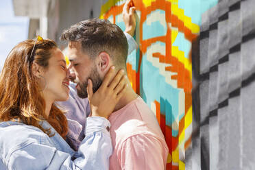 Paar küsst sich bei sonnigem Wetter an einer Grafittiwand - IFRF00820
